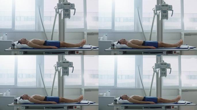 在医院里，一名男子坐在床上等待x光机扫描他的腿是否受伤。扫描骨折、四肢骨折、癌症或肿瘤。拥有技术先进