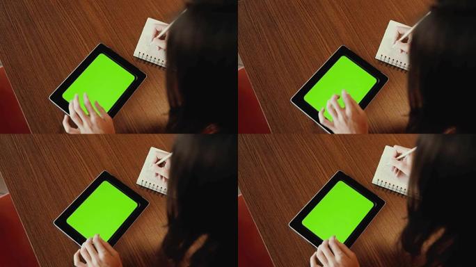在平板电脑上工作的女人做笔记。绿屏