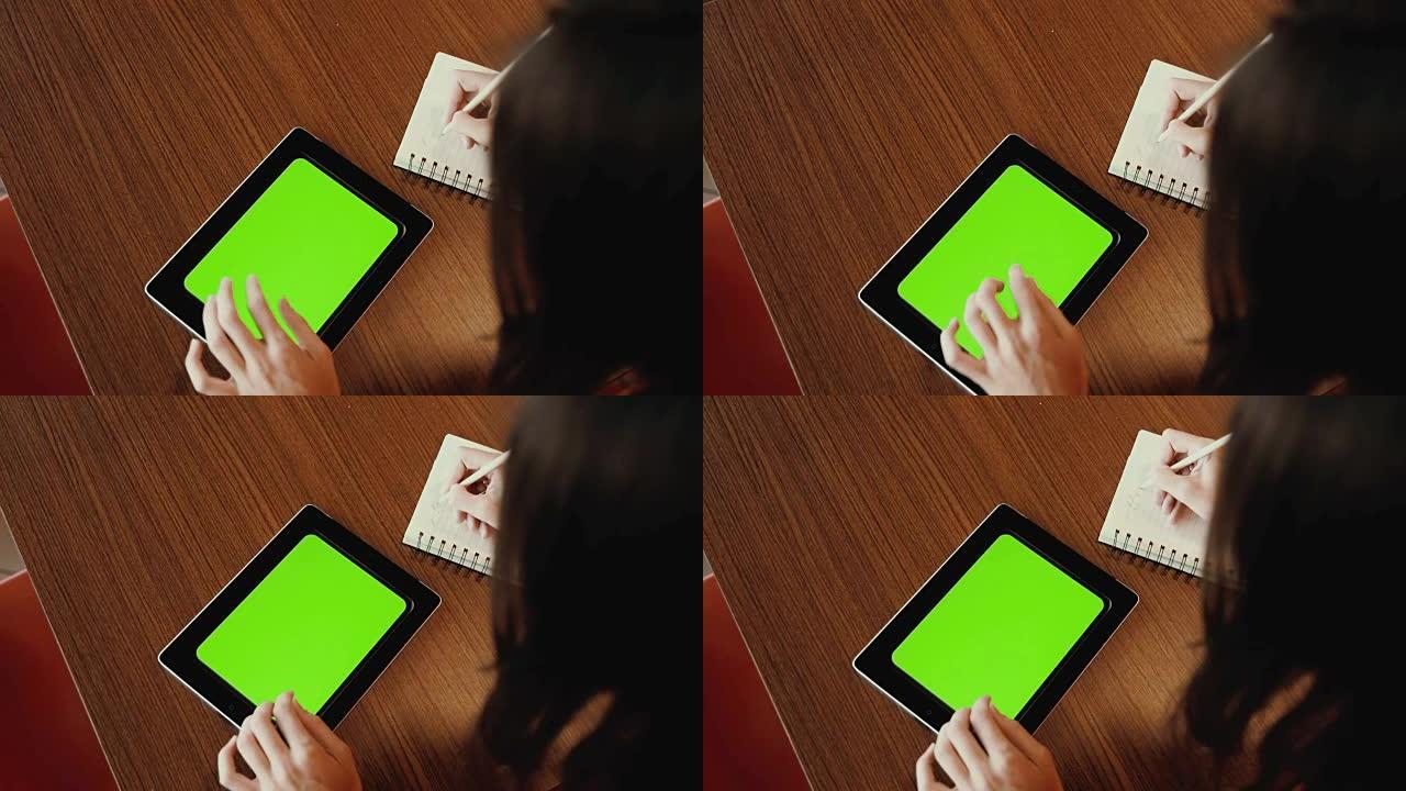 在平板电脑上工作的女人做笔记。绿屏