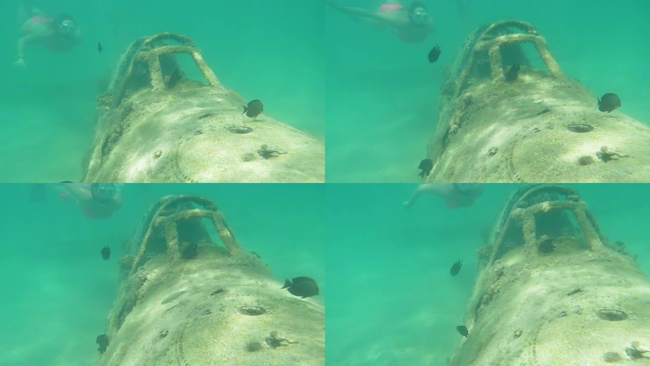 水下: 吸引女人的浮潜朝着飞机周围游动的黑鱼
