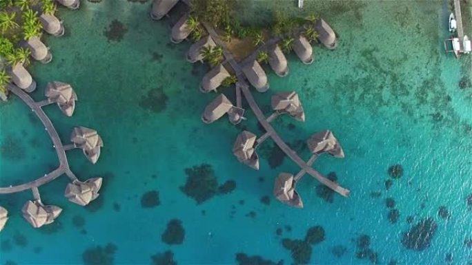 空中: 在高级酒店度假村的豪华昂贵的水上平房别墅上方飞行，带有宽敞的私人房间，面对阳光明媚的热带岛屿