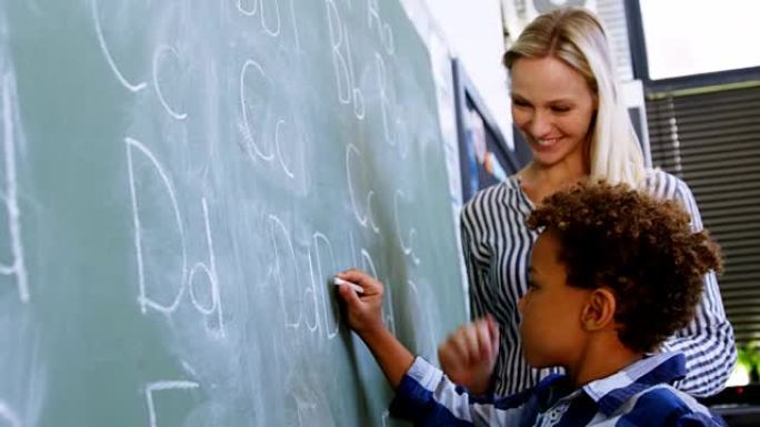 老师协助男生在黑板上写字母