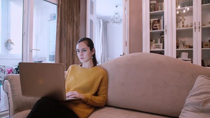 美丽的女孩坐在沙发上使用笔记本电脑在家在客厅