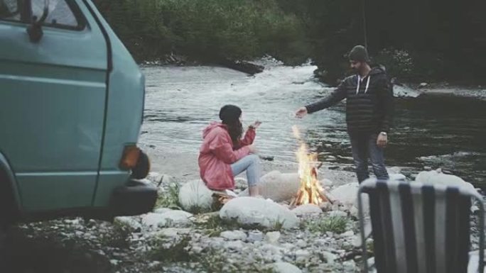 年轻夫妇在炉火旁放松。露营者在后台。山地景观