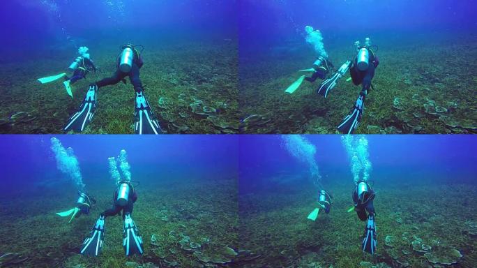 慢动作: 在蓝色清澈的水中游泳的水肺潜水员的水下拍摄。