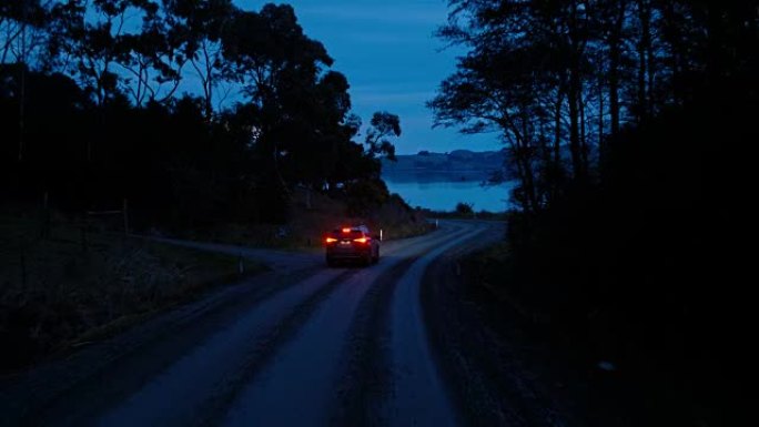 鸟瞰车在乡间小路上行驶，越野车在黄昏时驾驶，大灯穿过松树