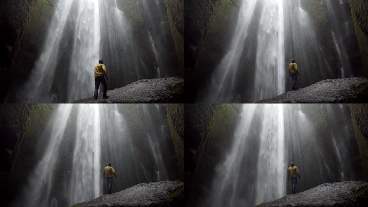 大风天，年轻人站在冰岛强大的瀑布gljufragui附近的石头上的后景