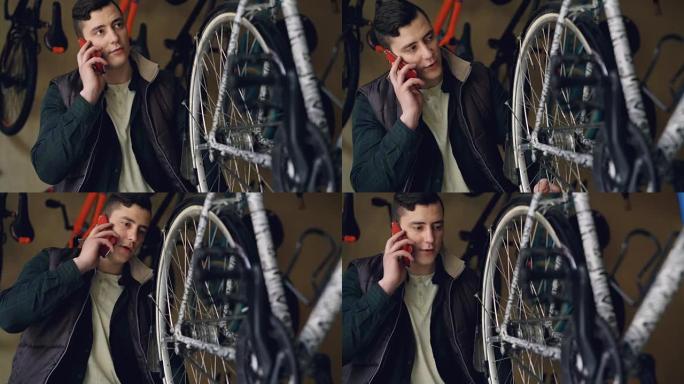 严肃的年轻人自行车修理工正在用手机说话时检查和转动车轮。自行车维护、沟通和专业理念。
