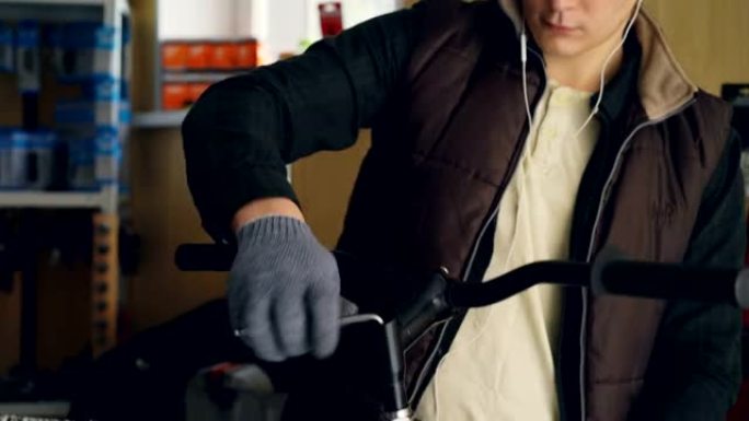 青少年专业修理工的倾斜拍摄耳机用内六角扳手固定自行车车把，用手戴防护手套握住方向盘。