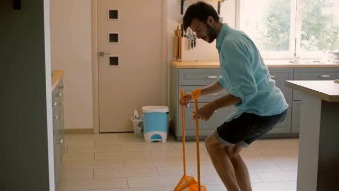 年轻人，丈夫在厨房扫地时用黄色扫帚闲逛。慢镜头，稳定镜头