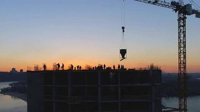 日落时用起重机和工人对建筑工地进行空中拍摄