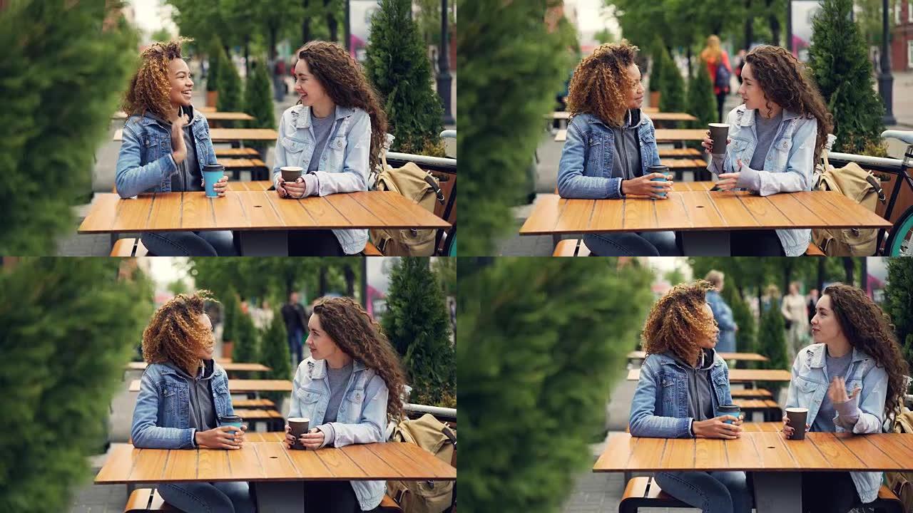 开朗的年轻女性最好的朋友坐在户外咖啡馆的餐桌旁喝咖啡时笑着说话，女孩们正在社交，讨论新闻很开心。