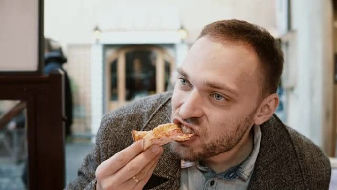 年轻英俊的女人拿着一片披萨咬它。饥饿的人在快餐店吃晚饭