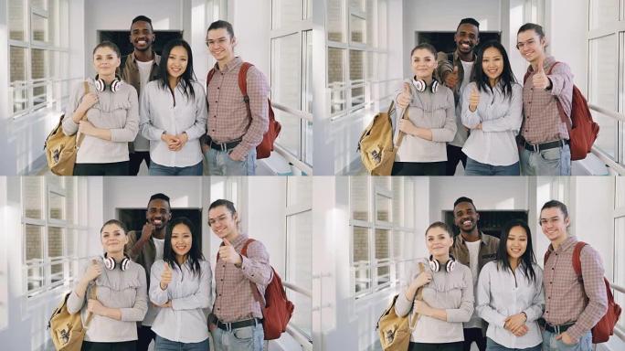 四名积极的多民族男女学生的肖像站在大学宽敞的白色走廊上看着相机竖起大拇指