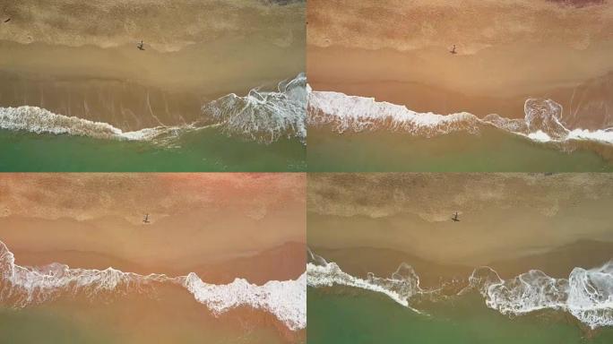 空中自上而下的冲浪者手里拿着冲浪板，沿着沙滩散步