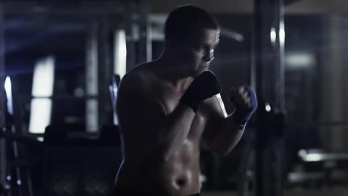 职业男拳击手正在黑暗的健身房训练拳打脚踢。