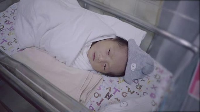 新生的亚洲婴儿用婴儿毯睡在孵化器里。