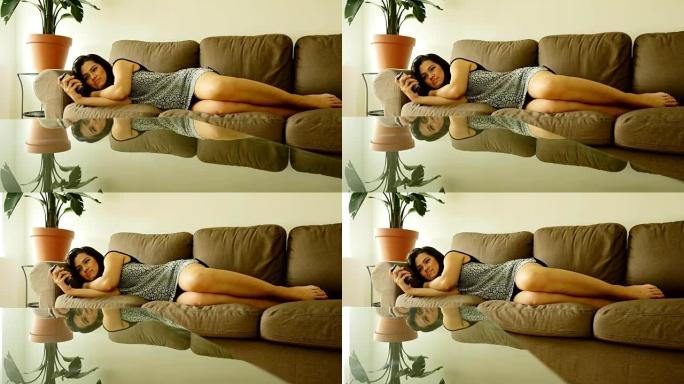迷人的亚洲女人躺在她家的沙发上。使用智能手机和发送短信。