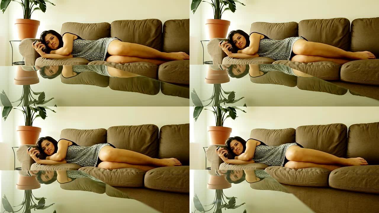 迷人的亚洲女人躺在她家的沙发上。使用智能手机和发送短信。