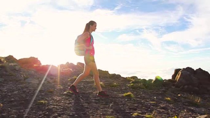 背包徒步旅行者带着太阳耀斑在山顶徒步旅行。年轻健康的女人在大自然中的冒险。