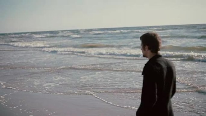 一个年轻人在大风天沿着美丽的海滩散步，手里拿着鞋子