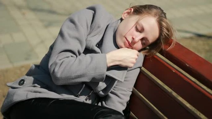 一个年轻女人穿着衣服睡在户外的长椅上。