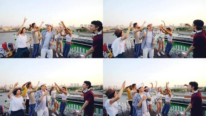 当酷酷的DJ在夏日的屋顶派对上与调音台一起工作时，年轻男女的慢动作跳舞和大笑。娱乐、青春和音乐概念。