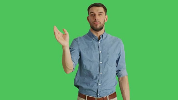 一个休闲男子站在绿屏背景上挥动和触摸手势的中等镜头。