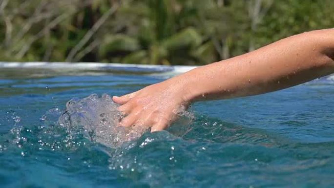 关闭女性手触摸水面溅水滴在游泳池和水疗度假村