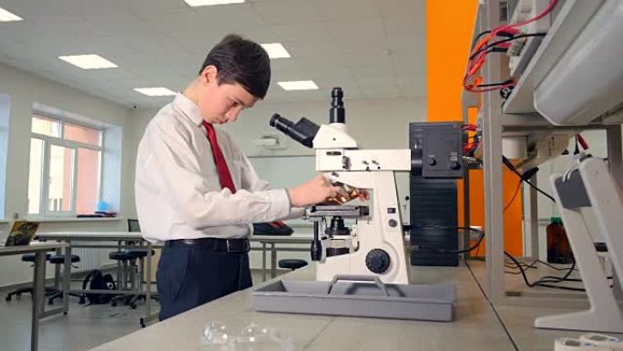 中学男孩在学校实验室的显微镜下进行生物学研究。