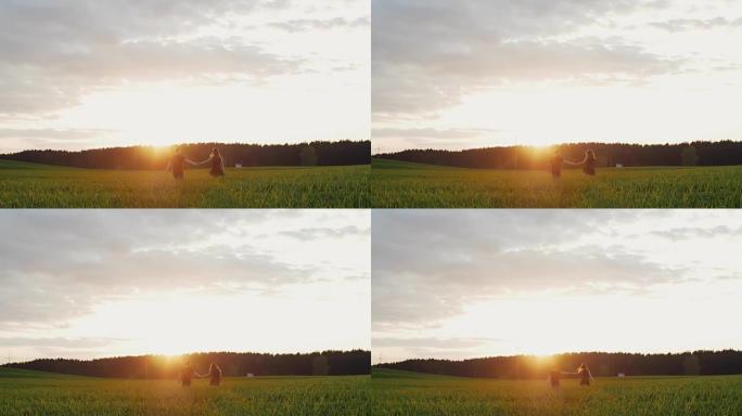 日落时分，年轻夫妇在田野里散步的美丽背景图。他们远离相机，牵着手。慢mo
