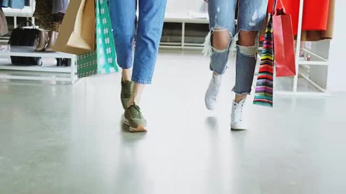 特写镜头多莉拍摄的女性双腿在豪华商店中缓慢行走。妇女穿着牛仔裤和运动鞋，背着明亮的纸袋。