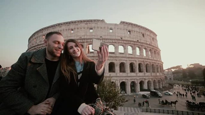 幸福的年轻夫妇在意大利罗马竞技场附近自拍。英俊的男人亲吻女人，微笑