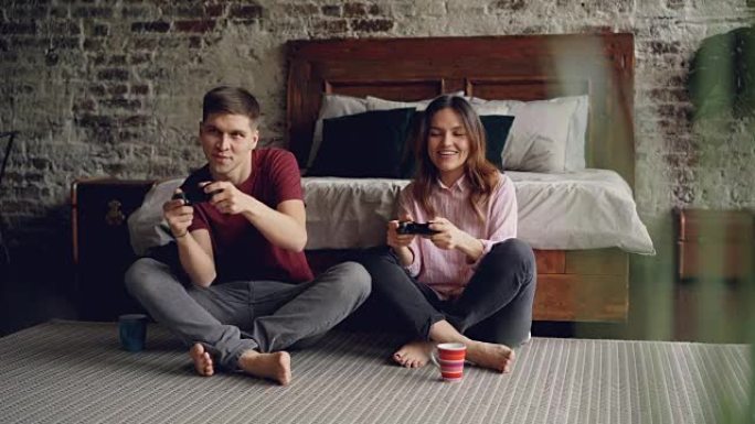 丈夫和妻子坐在家里的卧室地板上拿着操纵杆玩电子游戏，男人赢了，女人输了，两个人都在享受游戏。