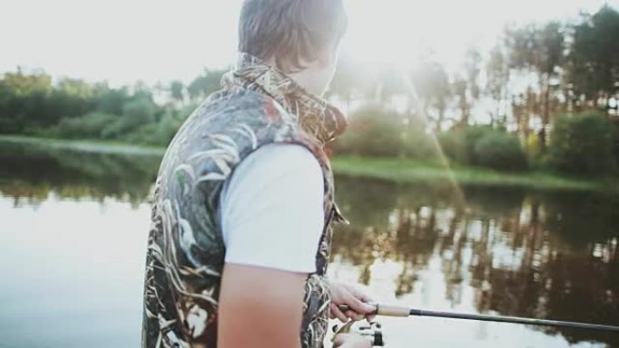 年轻人坐在橡皮船上，在湖边钓鱼。雄性将钩子扔进水中并扭动卷轴