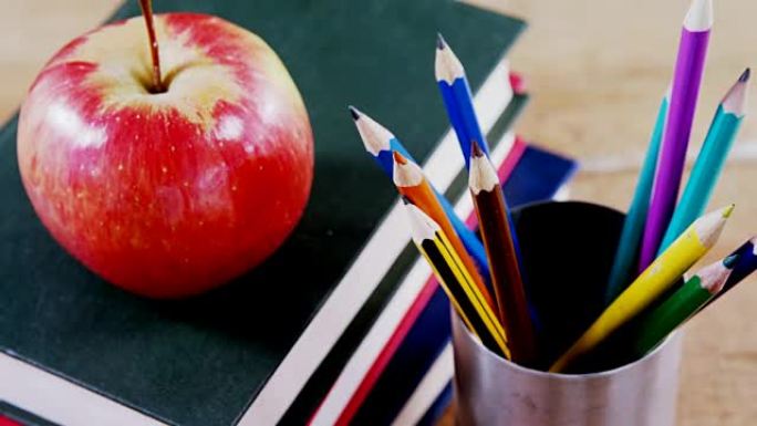 苹果在书堆上，桌上有彩色铅笔