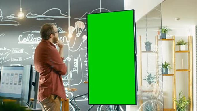 男性开发人员看着带有模拟绿屏的交互式白板。他抚平胡须，思考问题解决方案。在带有黑板墙的背景创意办公室