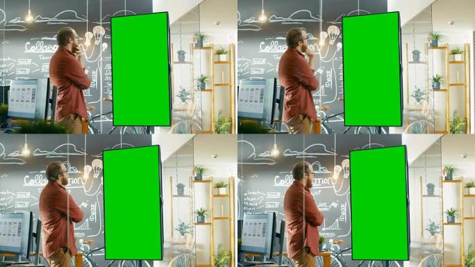 男性开发人员看着带有模拟绿屏的交互式白板。他抚平胡须，思考问题解决方案。在带有黑板墙的背景创意办公室