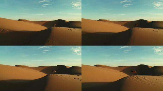 日落时分在沙漠沙丘中隔离的彩色沙滩伞的空中飞行