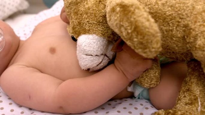 婴儿躺在婴儿床吮吸安抚他人抱着泰迪