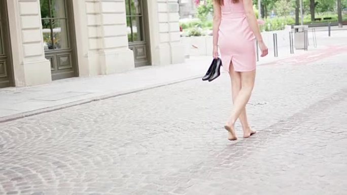 年轻的女人手里拿着高跟鞋，松了一口气。在城市中漫步