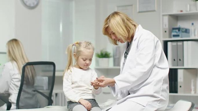 女医生正在检查一个小女孩的手。护士在后台工作。