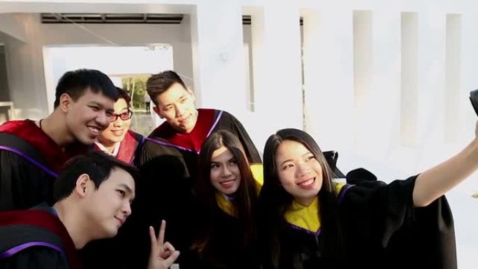 一群穿着砂浆板和单身汉礼服的快乐国际学生，带着文凭在户外用小型相机自拍。教育、毕业、技术和人的概念。