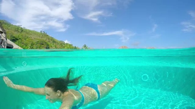 慢动作: 女人在水下游泳池游泳，背景中的水上别墅