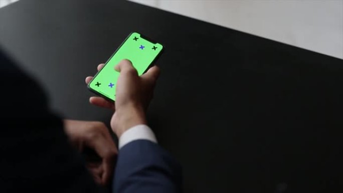 男性手持绿屏智能手机。男子站在窗户附近时使用手机。点击触摸屏，上网。特写