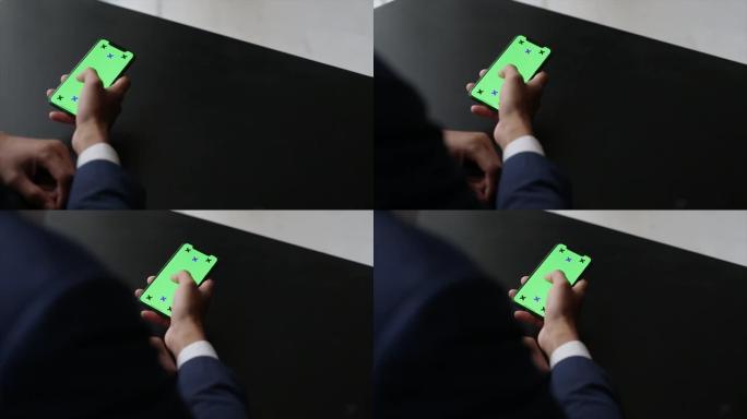 男性手持绿屏智能手机。男子站在窗户附近时使用手机。点击触摸屏，上网。特写