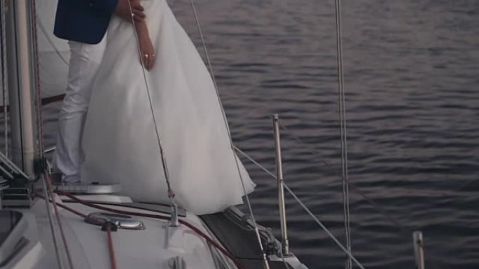 穿着婚纱的年轻夫妇站在游艇上的特写镜头。新娘和新郎晚上拥抱