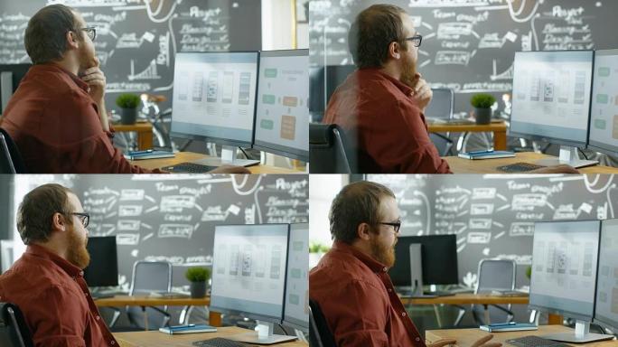 男性移动视频游戏应用程序开发人员在个人计算机上工作，设计线框，他在思考手势中抚平胡须。他在创意独立工