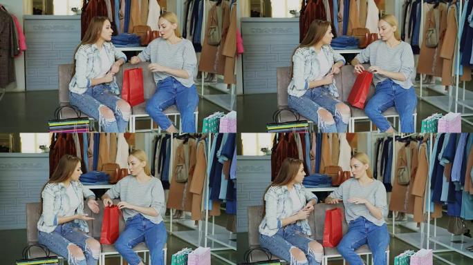 两名年轻女士坐在购物中心的服装部，购物后聊天。背景丰富的女装和购物袋。