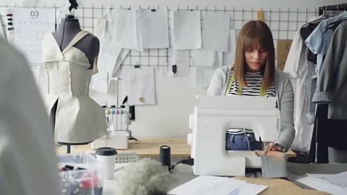 自雇服装设计师正在使用缝纫机，缝制纺织品并查看工作室桌子上的草图。裁缝店概念的日常工作。